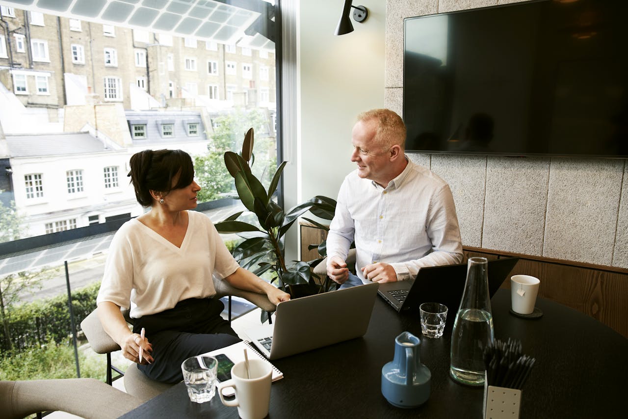 Services-02 Two business professionals engaging in a team meeting in a modern London office with a large window view.