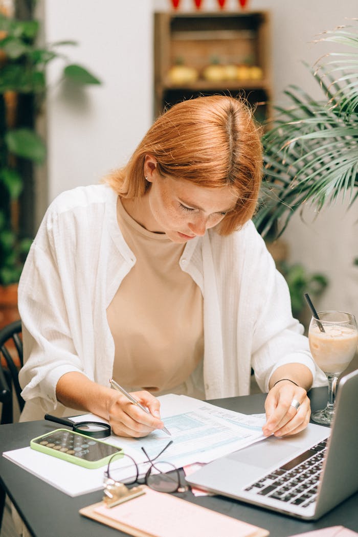 digital-01 Woman analyzing financial documents using laptop and calculator indoors.
